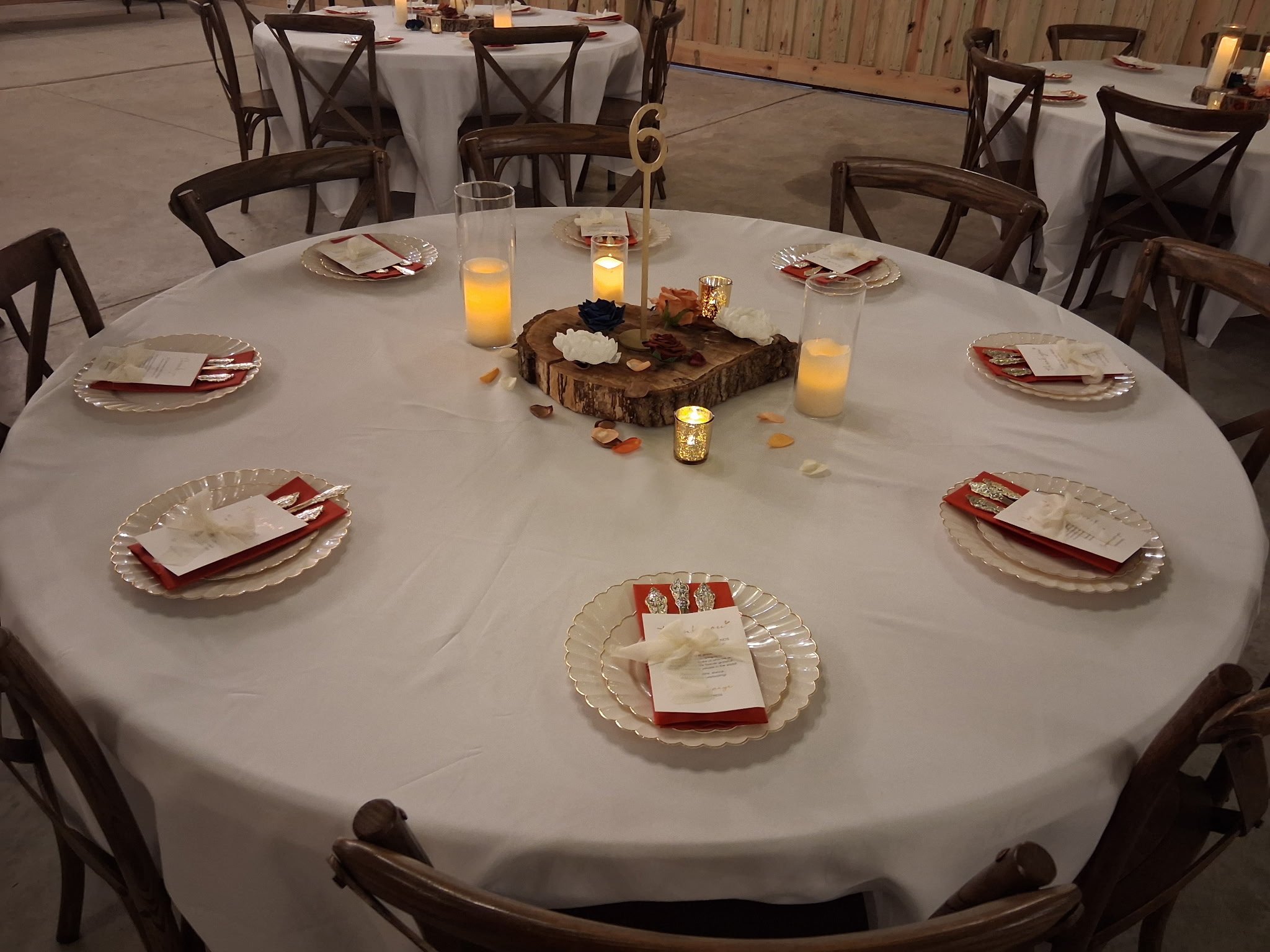 Rustic wedding table with white linens, red napkins, and a wood-slice candle centerpiece