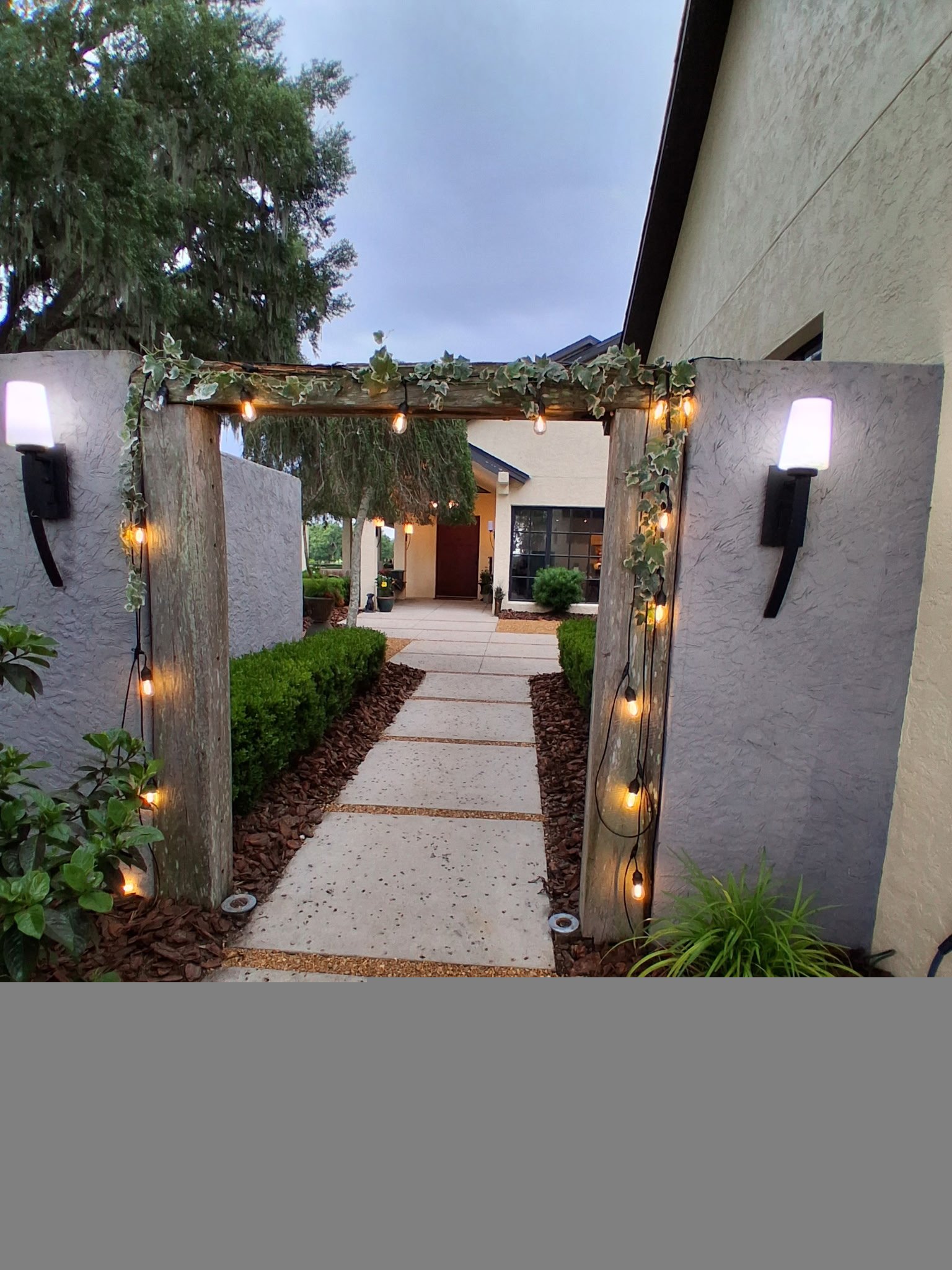 Wooden venue entrance arch draped with warm string lights and greenery at dusk