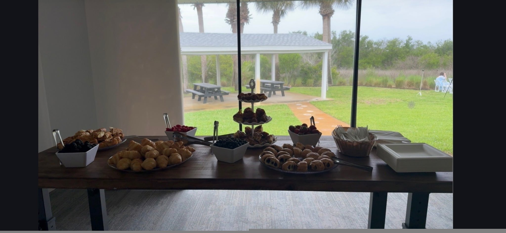 Buffet of pastries and fruit overlooking an outdoor pavilion and lawn
