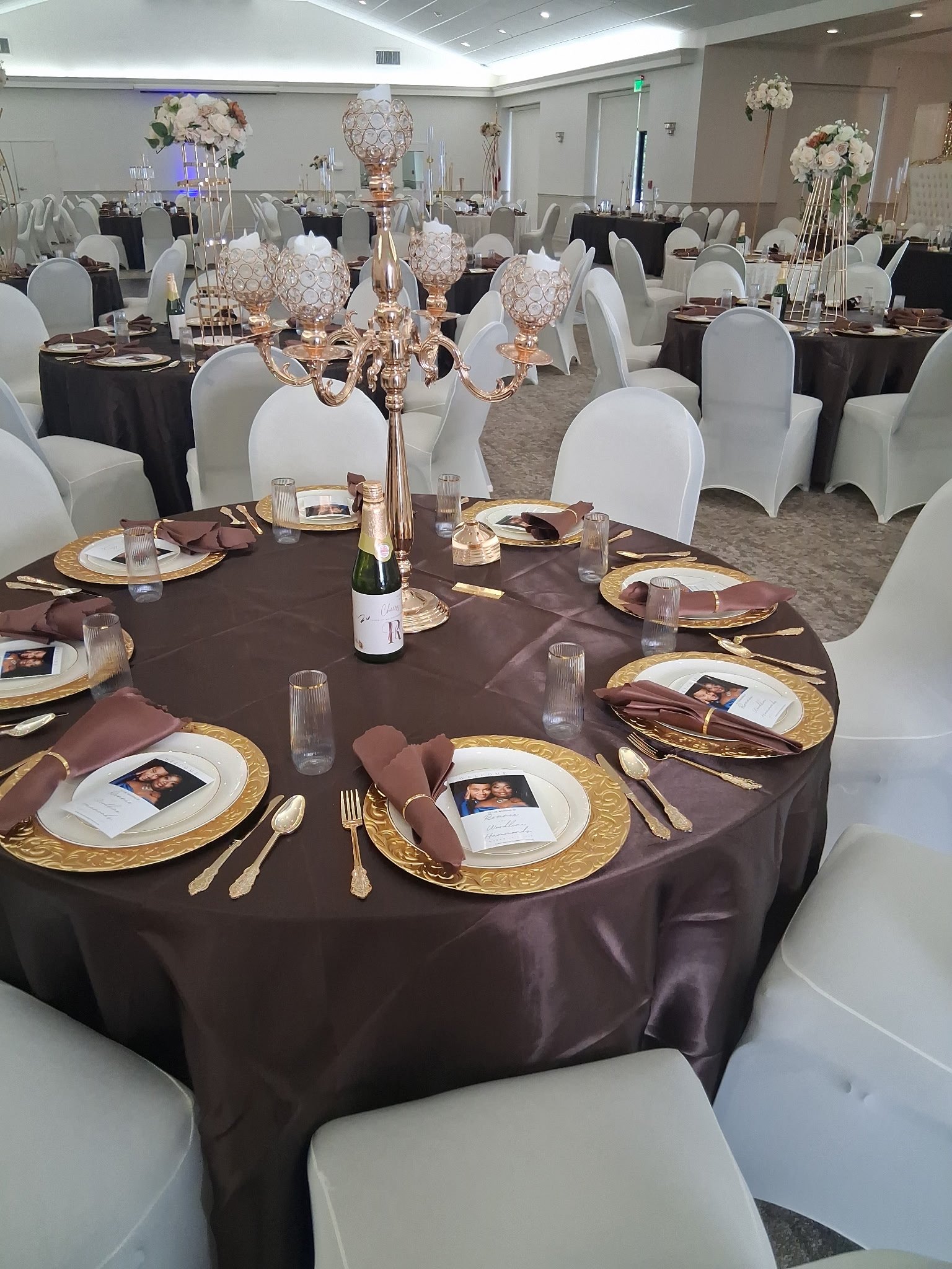 Formal reception table with chocolate satin linens, gold chargers, and a tall gold candelabra