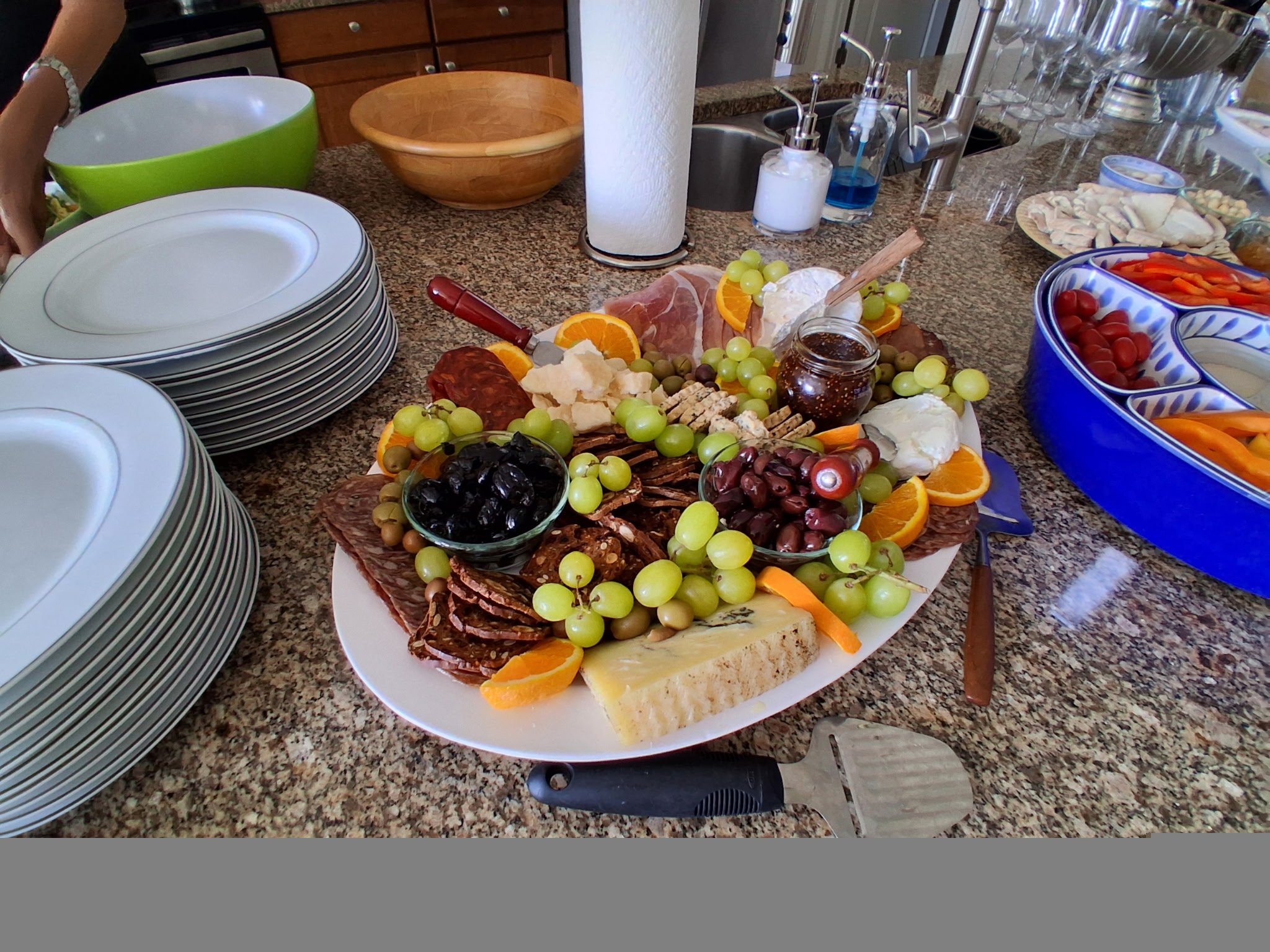 Charcuterie board with grapes, meats, and cheeses beside stacks of white plates