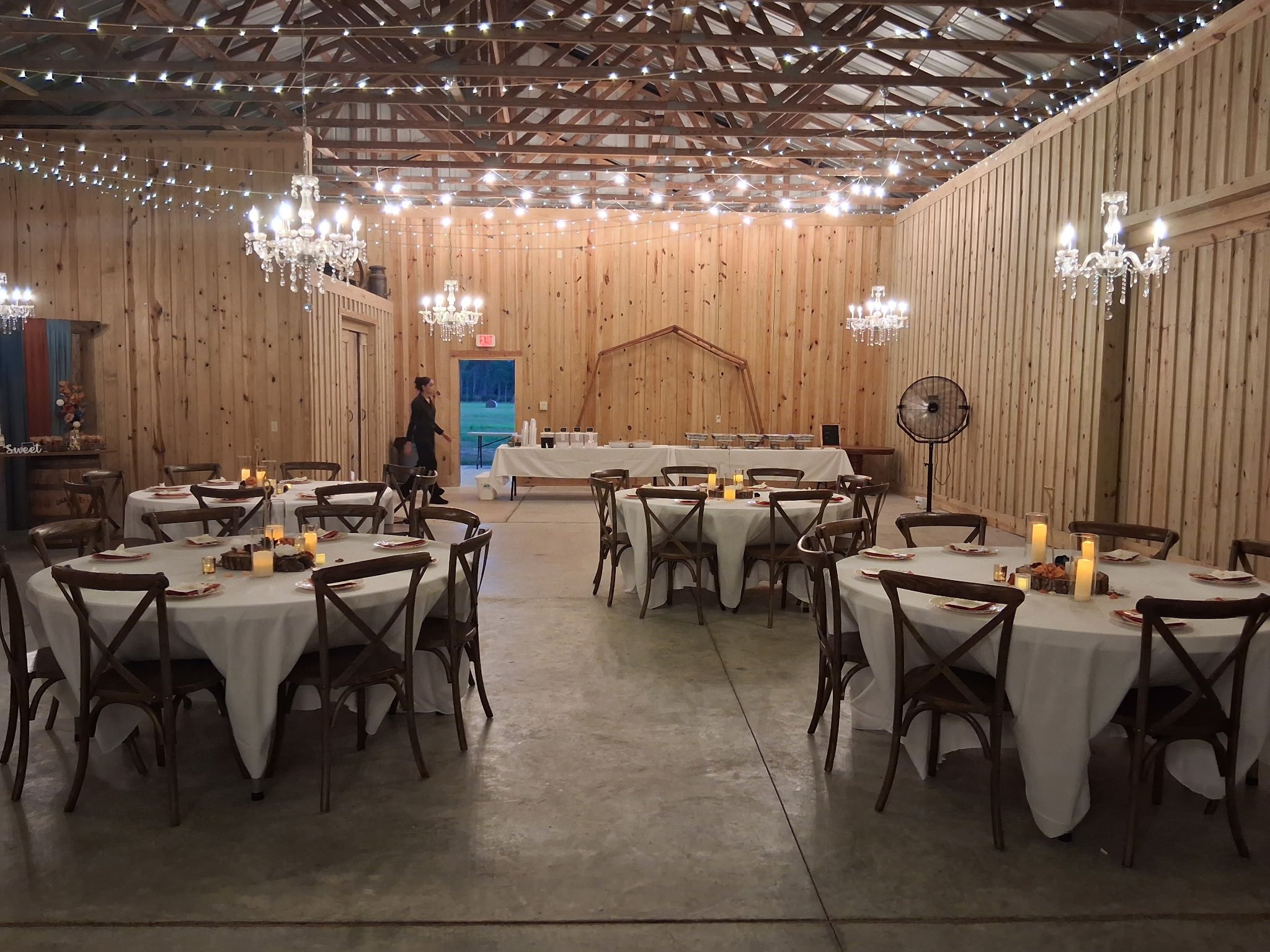 Barn reception hall with round tables, white linens, and crystal chandeliers